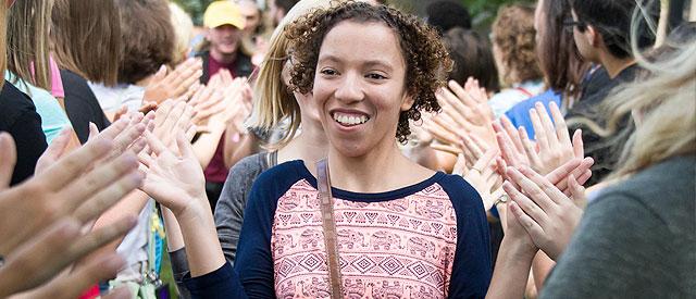 Joyful woman walking through a clapping crowd, feeling celebrated and supported.